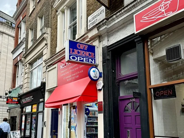 Une vue de rue montrant des devantures de magasins dont une épicerie sur Aldersgate Street.