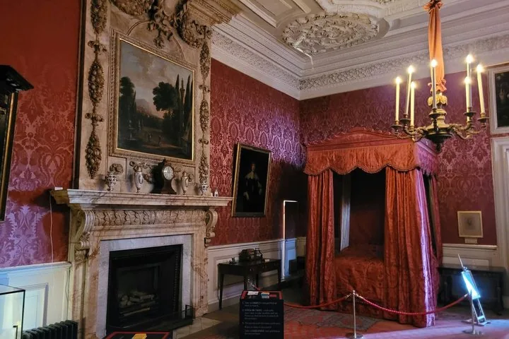 An ornate room interior with a four-poster bed and patterned red wallpaper.